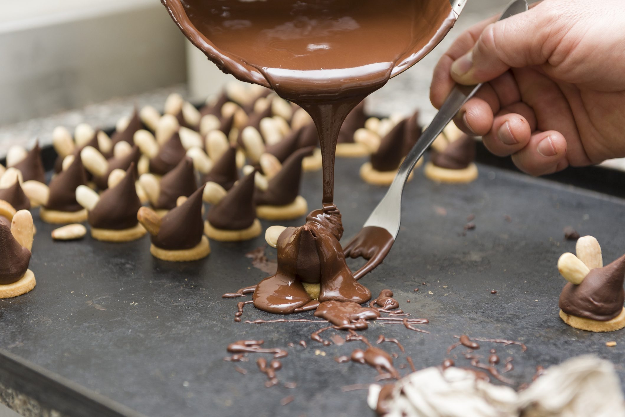 confectioner Pouring chocolate over almond-topped cookies.